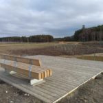 Photo of a new bench on a wooden platform beside a pond