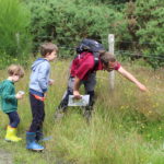 Photograph of Warden Andi pointing out a butterfly yo two attentive children