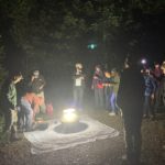 Photo of people standing around a light in the dark.