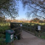 Photo of the entrance showing a poo bin beside a bridge