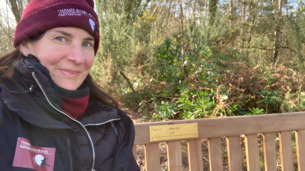 Photo of Warden Nicky sitting on the bench. There's an "After Life" brass plague on the back rest.