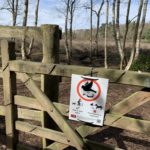 Photo of a sign tied to a gate asking dog owners to keep to main paths