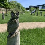 Photo of a carved owl, with natural play equipment in the background.