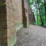 Photo shows a large brick built wall in the woodlands.