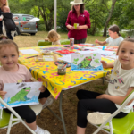 Two young girls holding up their paintings of frogs.