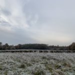 Photo of a large frosted meadow with hay bales stacked up.