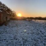 Photo of a hillside with frost on the ground and the sun setting behind a pill box.