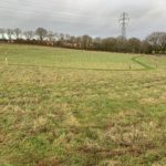 Photo of a sloping field with mown paths and a pylon carrying overhead wires.