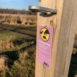 Photo of a fencepost with a pink and yellow sign warning visitors that there are grazing animals.