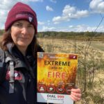 Photo of Nicky in her uniform, holding up a sign that reminds us about fire risk.