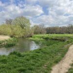 Photo of a spring scene, with a river flowing through a meadow and a rough path running along side.