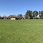 Photo of a large recreation field, with a wooden building in the distance.