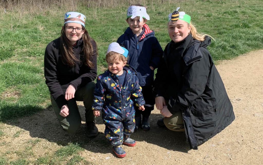 Photo of two small boys with wardens Kay & Zoe, all wearing colouring cardboard head bands!
