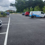 Photo of a large, tarmac car park. White lines clearly mark out parking spaces. A few cars are parked.