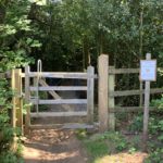 Photo of a wooden gateway, leading to a path. A sign asks for dogs on leads.