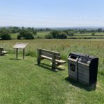 Photo take from the top of the meadow where two benches are placed to look out over the surrounding countryside. There is also a dog poo bin here and a notice board (currently blank).