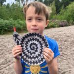 Photo of a small boy holding up a colied cardboard snake complete with bright red tongue.