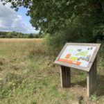 Photo looking across a meadow. An information board stands in the foreground.