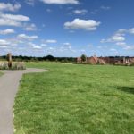 Photo of a tarmac path that goes across a grassy area on the edge of a housing development.