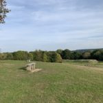 Photo looking across the slopes of a green knoll. Two benches are positioned at the top.