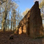 Photo shows a tall, brick built firing wall standing amongst the trees.