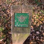Photo of a brass plaque showing a bumble bee, mounted on top of a short post.