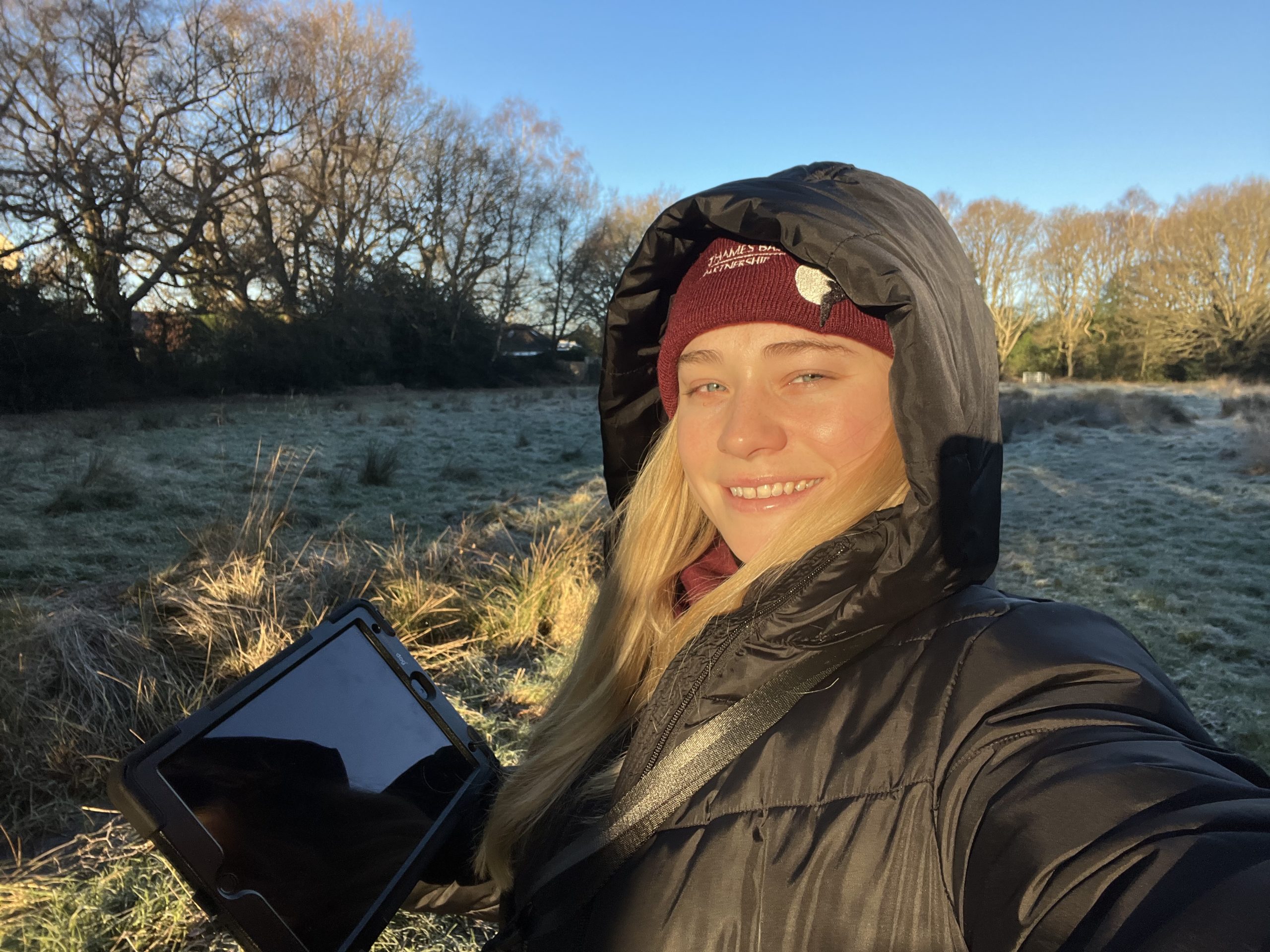 Senior warden Zoe, dressed in black, facing the sun while standing in a frosty meadow with bright blue sky behind