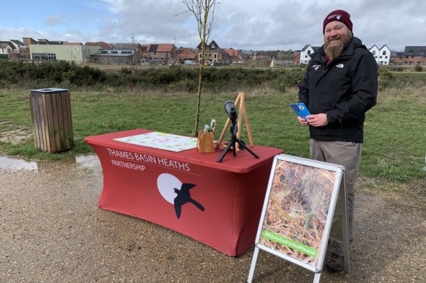 Photo of Warden Richard beside a sign with a photo of a Woodlark nesting on the ground.