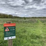 Photo of the green meadow with a sign in the foreground. It says "Ground Nesting Skylarks March 1st - August 31st"