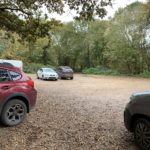 Photo of a rough, earth car park surrounded by trees.