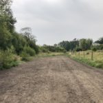 Photo of a bare ground path bordered by trees and a post and wire fence
