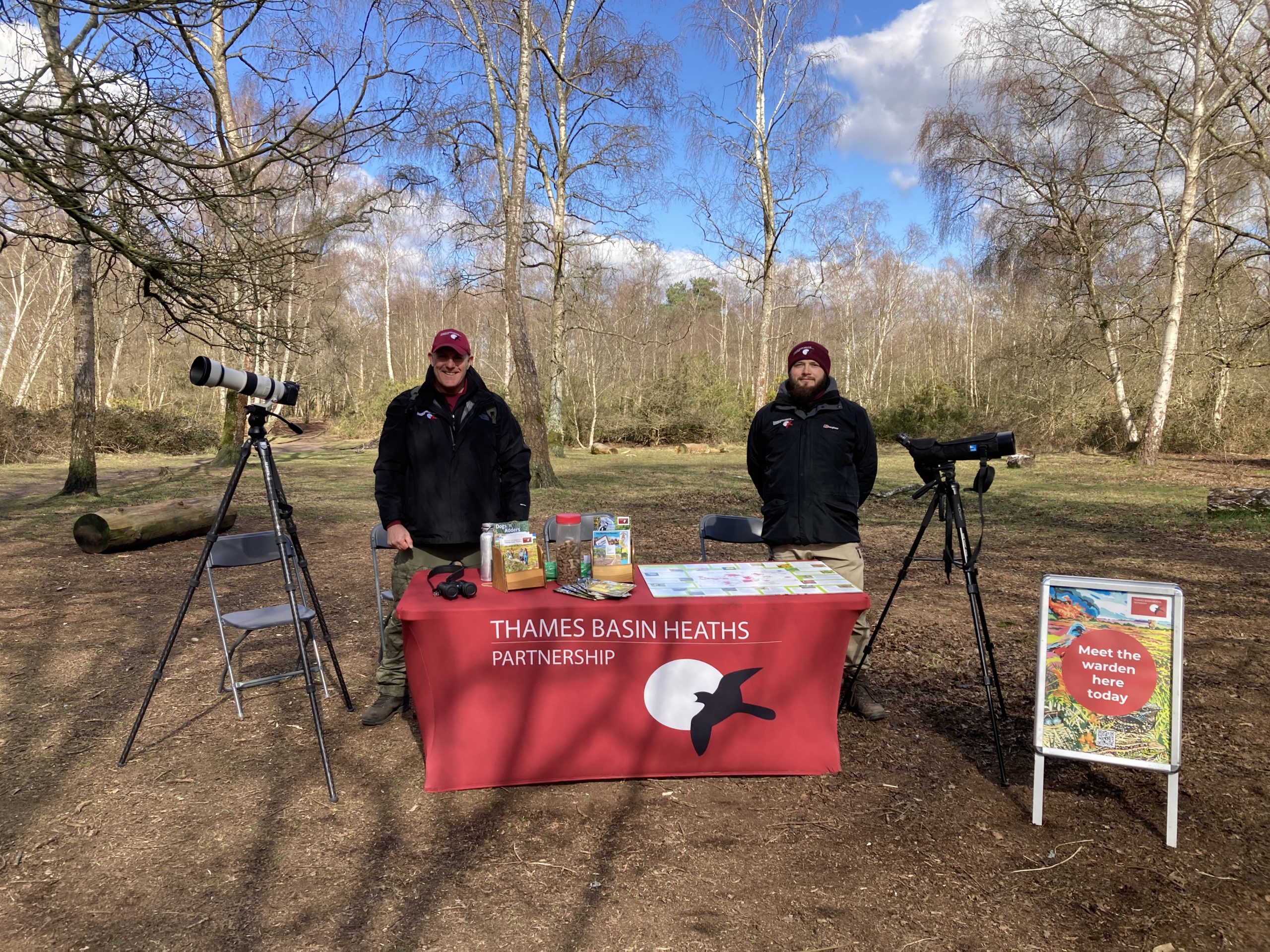 Two wardens by a heathland pop up table with a telescope and camera.